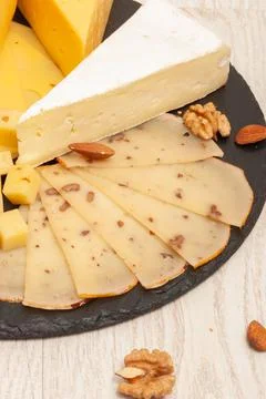 Different types of cheese on a black graphite board with dried apricots, walnuts Stock Photos