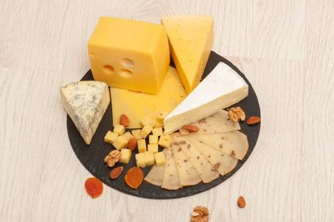 Different types of cheese on a black graphite board with dried apricots, walnuts Stock Photos