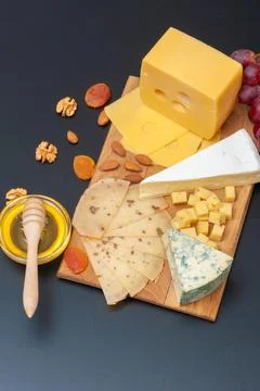 Different types of cheese on a black graphite board with dried apricots, walnuts Stock Photos