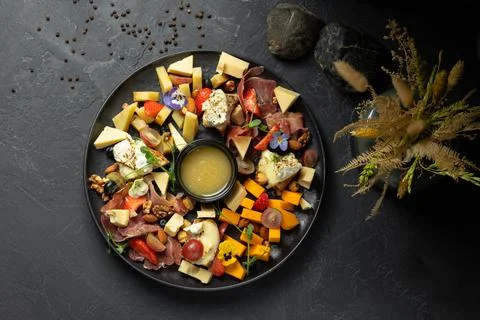 Different types of cheese with fruits, nuts and meat with sauce on a black plate Stock Photos