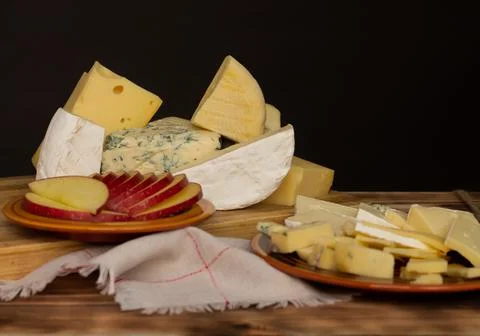 Different types of cheese on a rustic wooden cutting board on a dark backgrou Stock Photos