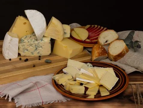Different types of cheese on a rustic wooden cutting board on a dark backgrou Stock Photos