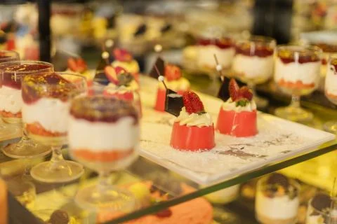 Different types of desserts are arranged neatly on a glass shelf in a bakery. Stock Photos