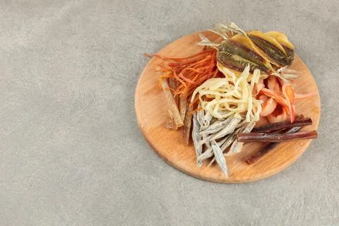 Different types of dried fish and squid on a round wooden board. Beer snack Stock Photos