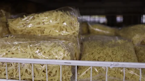 Different types of dry pasta in clear bags displayed on a grocery store shelf Stock Footage 345978906