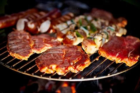 Different types of juicy meats on hot coals on grill in garden Stock Photos