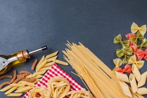 Different types of pasta and bottle of olive oil on a black slate background Foto stock