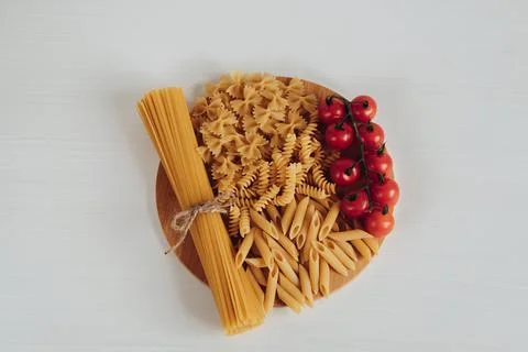 Different Types of Pasta and Cherry Tomatoes on the Tray on the White Background Stock Photos
