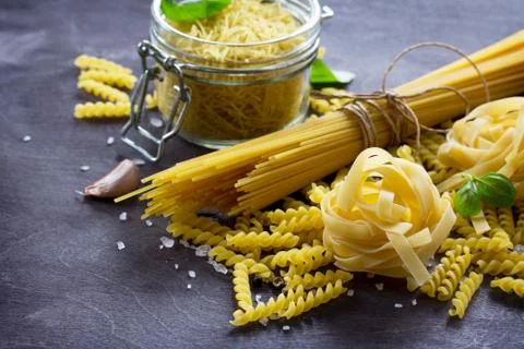 Different types of pasta with basil on the kitchen wooden table. Stock Photos