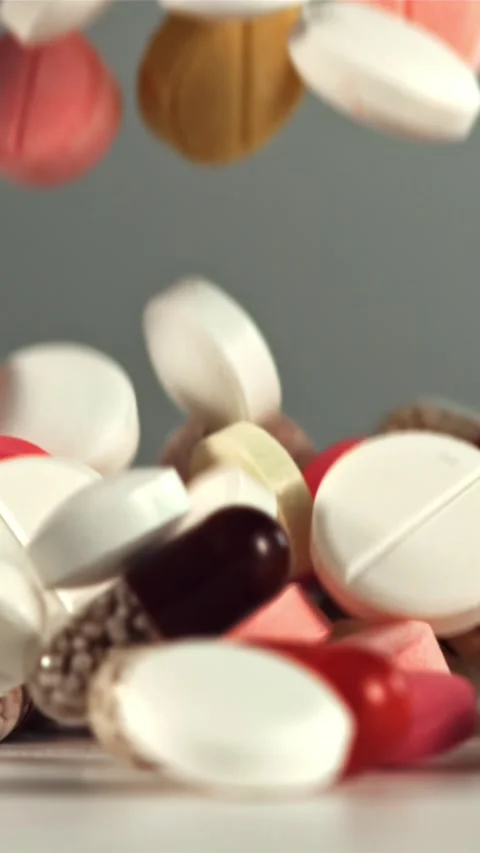 Different types of pills and capsules fall on the table. Filmed on a high-speed Stock Footage 335292229