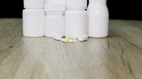Different types of pills are in front of white plastic pill bottles Stock Footage 325509257