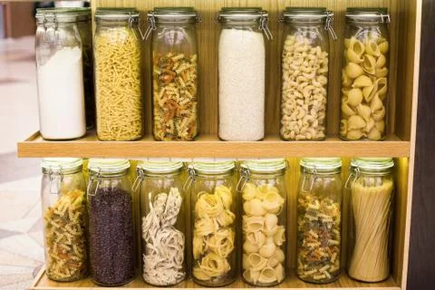 Different types of raw pasta in closed glass jars on the shelves. Showcase de Stock Photos