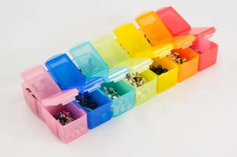 Different types of screws in small colored plastic containers. Stock Photos