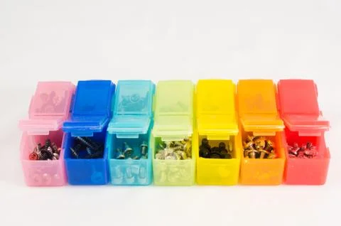 Different types of screws in small colored plastic containers. View close-u.. Stock Photos