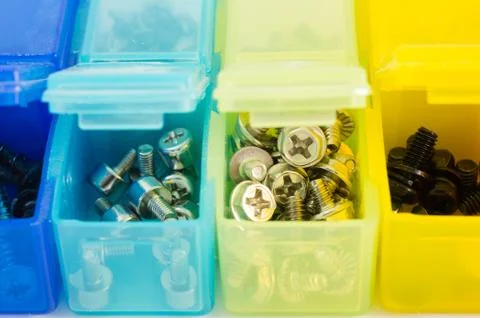 Different types of screws in small colored plastic containers. View close-u.. Stock Photos