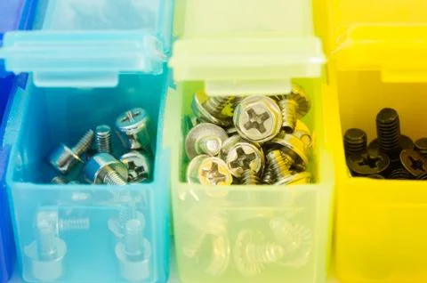 Different types of screws in small colored plastic containers. View close-u.. Stock Photos