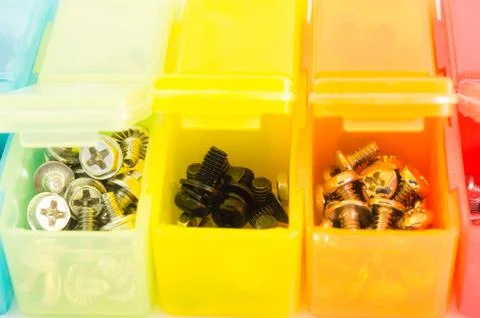 Different types of screws in small colored plastic containers. View close-u.. Stock Photos