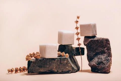 Different types of soap bars on stone pedestals with dry herbs on pink Stock Photos