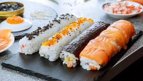 Different types of sushi rolls and ingredients on a black plate. Sushi is widely Stock Photos