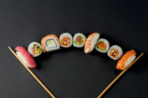 Different types of sushi rolls on a black background between chopsticks Stock Photos