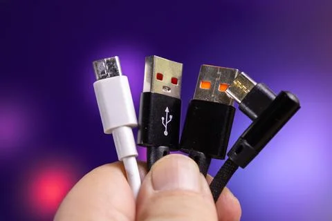 Different types of USB cables held by a person in a hand against a colored Stock Photos