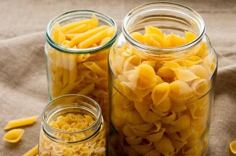 Different types of yellow macaroni pasta in glass bowl on hessian fabric clot Stock Photos