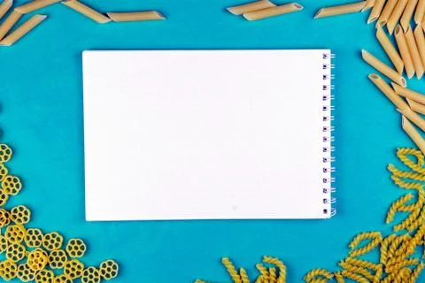 Different varieties of macaroni with a notebook on a blue background. Stock Photos