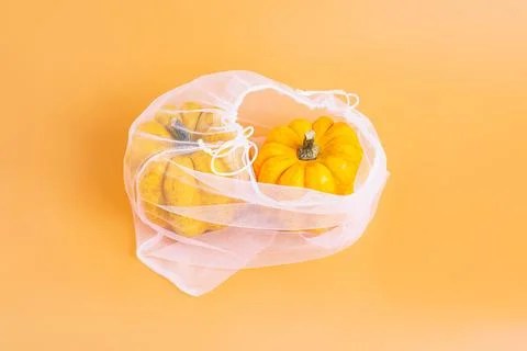Different varieties of Pumpkins in mesh bag of fabric on orange background Stock Illustration