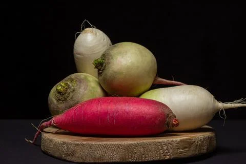Different varieties of radish on a black background. Long red radish next to whi Stock Photos