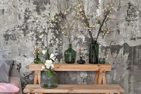 Different vases with spring flowers in front of grey concrete wall and a bed Stock Photos