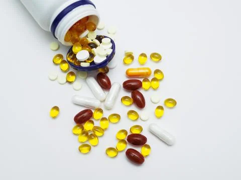 Different vitamins and tablets in capsules of different colors are poured from a Stock Photos