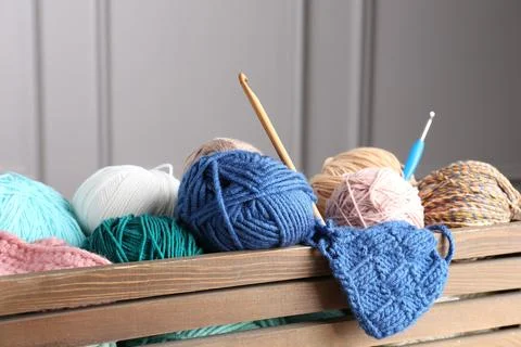 Different yarns, pattern sample and crochet hooks in wooden crate, closeup Stock Photos