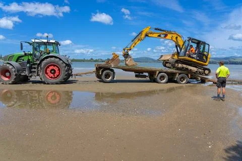 Digger on trailer behind tractor on beach. Fotos de archivo