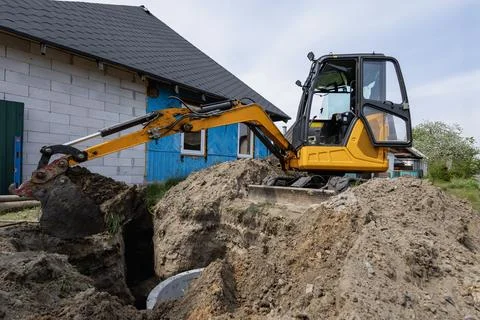 A digger is at work digging a hole beside a structure. The site shows signs o Stock Photos