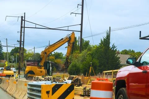 Digger is working on side of road while cars pass by there are construction m 스톡 사진