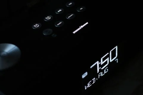 Digital alarm clock in darkness displaying 7:50pm wed aug 7 with buttons on top Stock Photos