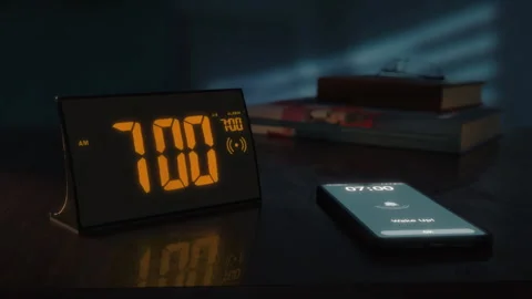 Digital alarm clock with orange clockface and the smartphone waking up at 7 AM Video stock 254784633