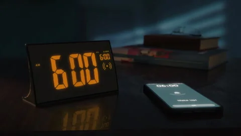 Digital alarm clock with orange clockface and the smartphone waking up at 6 AM Video stock 254784640