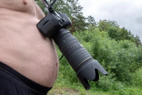 A digital camera with a large lens hangs around the neck of a big-bellied man Stock Photos