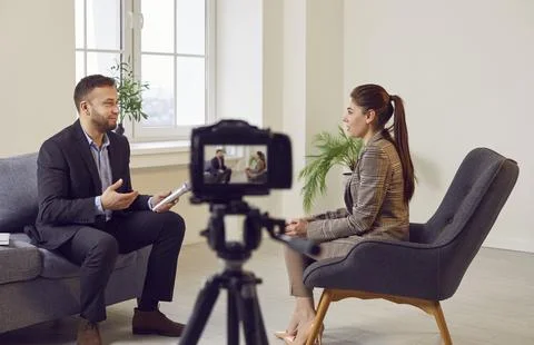 Digital camera on tripod recording interview of man and woman sitting and Stock Photos