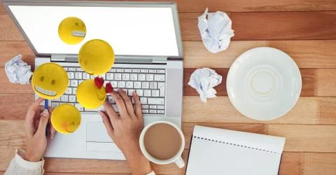 Digital composite image of hands using laptop while emojis flying over table Stock Photos