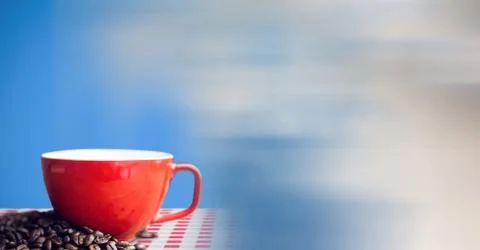 Digital composite of Red coffee cup on red and white table cloth with beans a Stock Photos