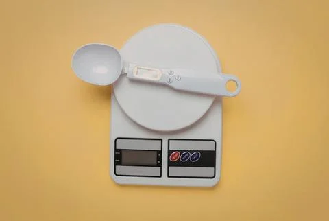 Digital kitchen scale with a white spoon on yellow background Stock Photos