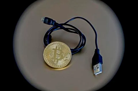 Digital kriptonite bitcoin with a USB cable on a bronze background. Stock Photos