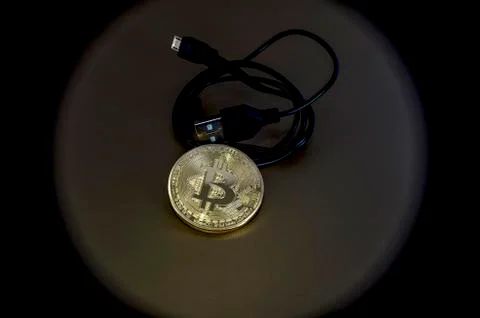 Digital kriptonite bitcoin with a USB cable on a bronze background. Stock Photos