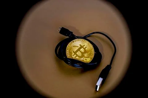 Digital kriptonite bitcoin with a USB cable on a bronze background. Stock Photos