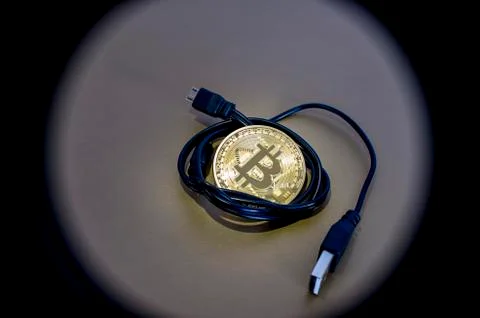 Digital kriptonite bitcoin with a USB cable on a bronze background. Stock Photos