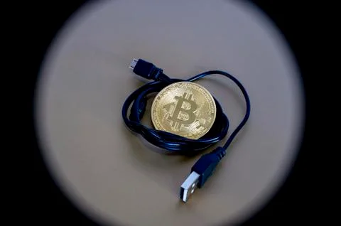 Digital kriptonite bitcoin with a USB cable on a bronze background. Stock Photos