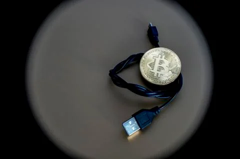 Digital kriptonite bitcoin with a USB cable on a bronze background. Stock Photos