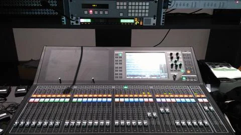 A digital mixing console with touchscreen, sliders, knobs, lights, and rack. Stock Photos